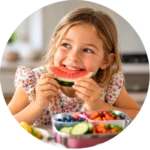 Young girl enjoying a slice of watermelon with a colourful lunchbox in front of her